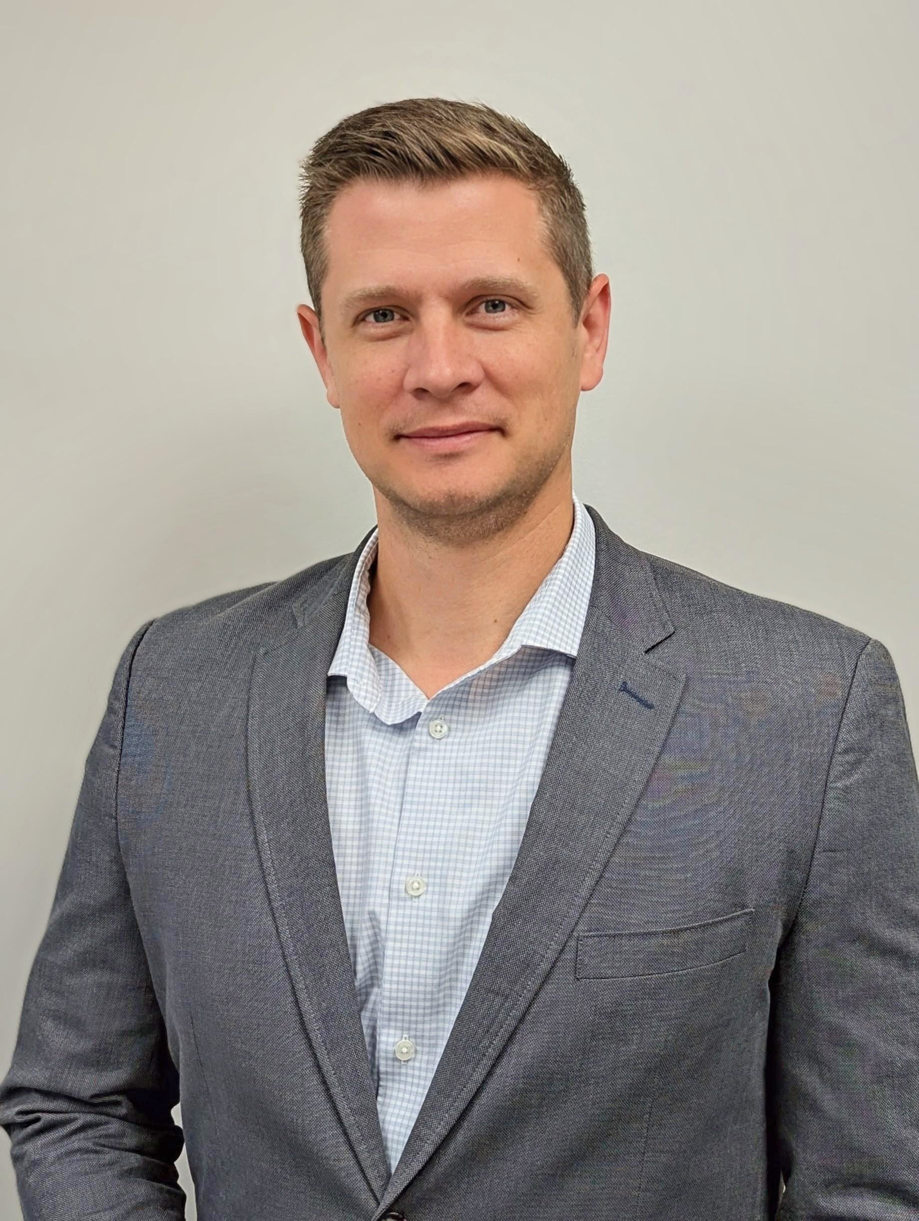 Professional portrait of a man wearing a gray blazer and pattered dress shirt