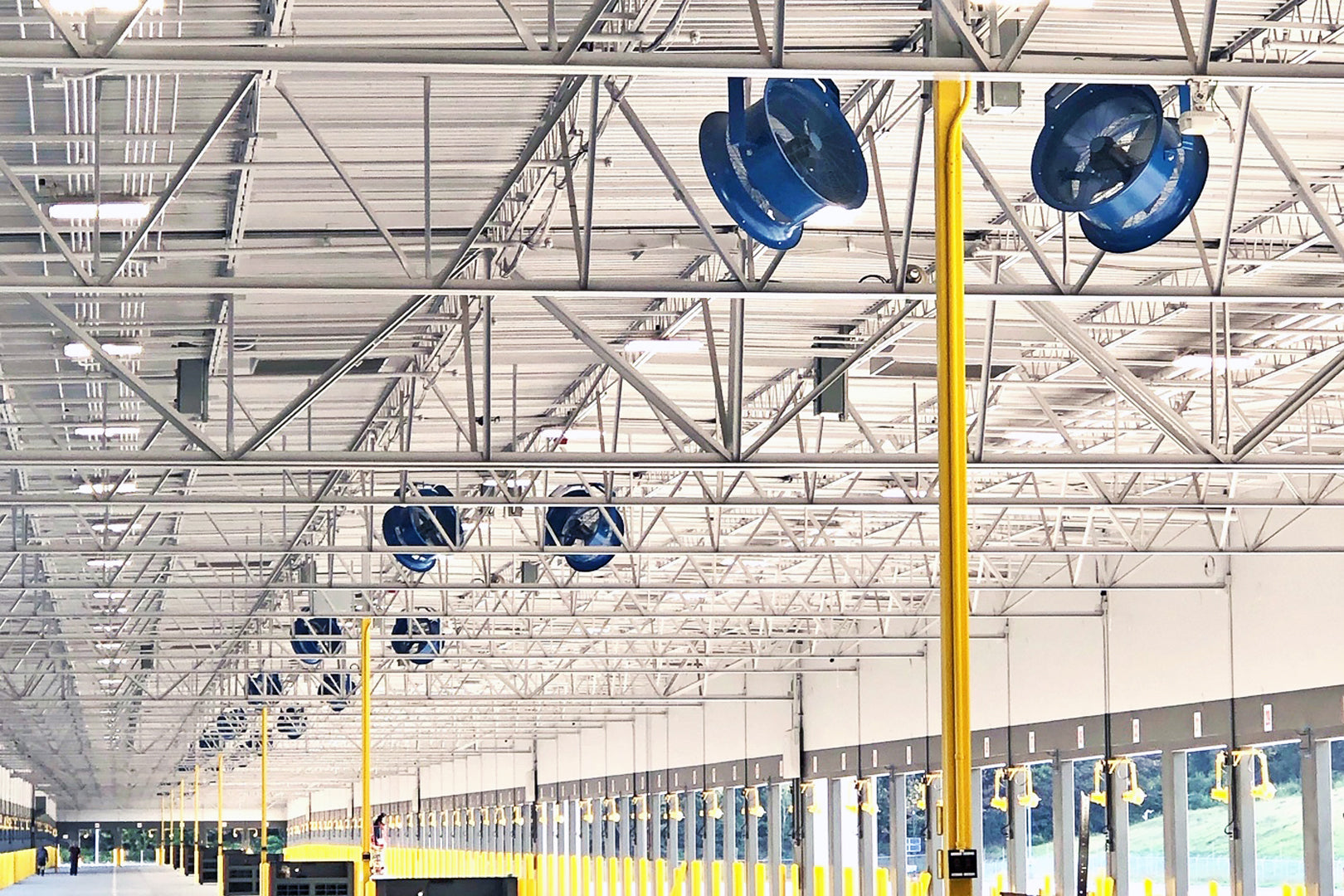 Multiple Patterson high-velocity warehouse fans mounted on ceiling trusses inside a large distribution center with loading dock bays