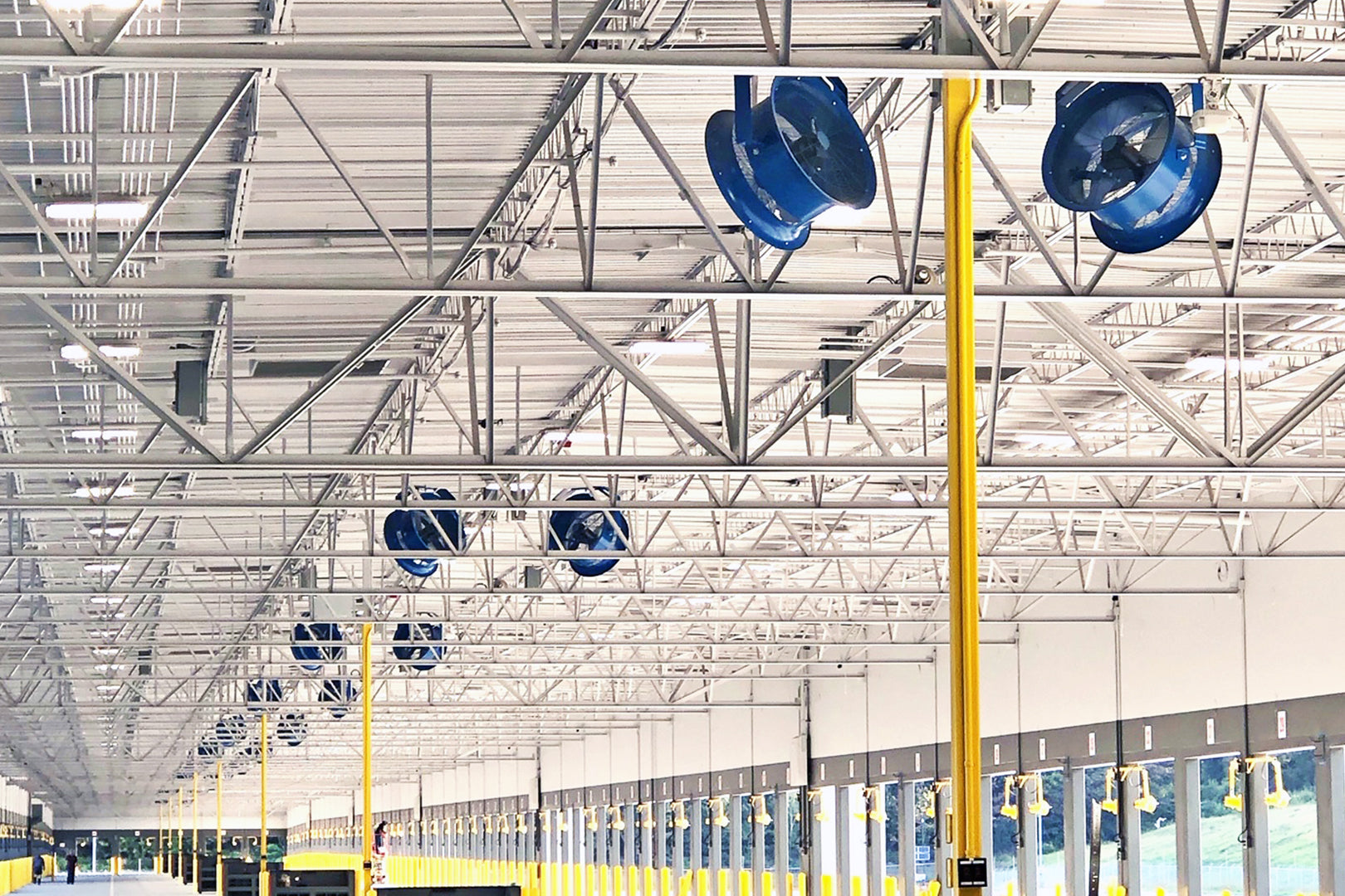 Rows of Patterson industrial warehouse fans mounted on ceiling beams inside a large cross-dock facility