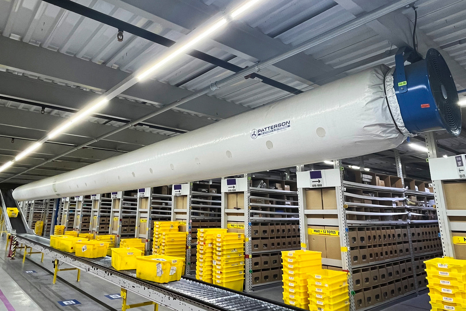 Patterson blower fan with long fabric air distribution tube installed over conveyor lines in a warehouse fulfillment center