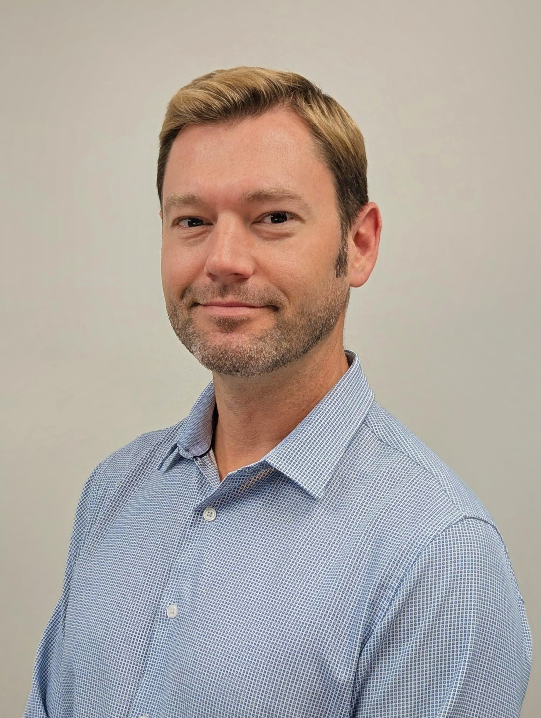 Professional headshot of a man wearing a light blue button-down shirt