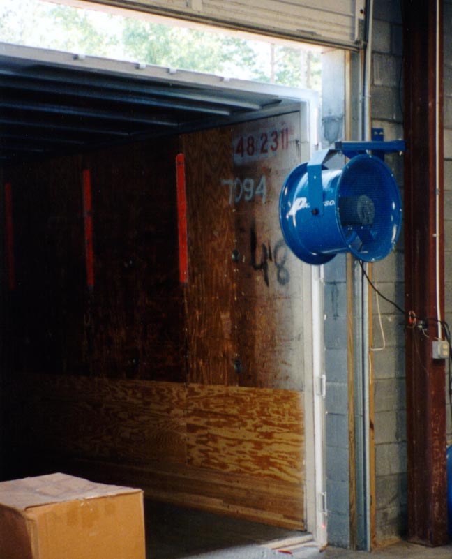 Blue warehouse loading dock fan mounted beside an open trailer door for improved airflow during loading operations