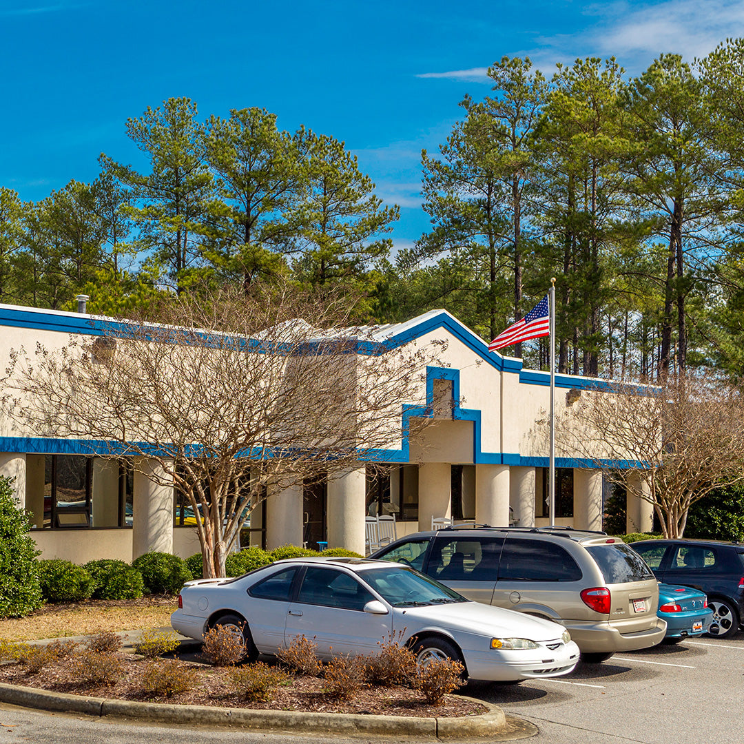 Exterior of the Patterson Fan corporate headquarters with blue trim, front parking area, and surrounding trees