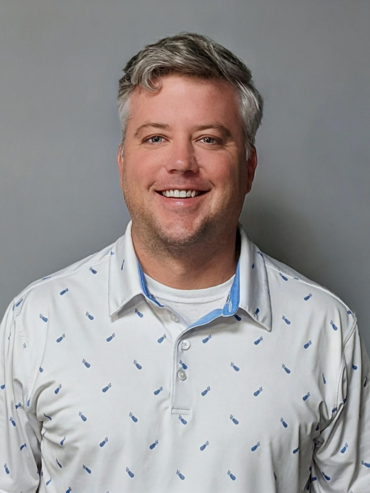 Professional headshot of a man wearing a light-colored patterned polo shirt