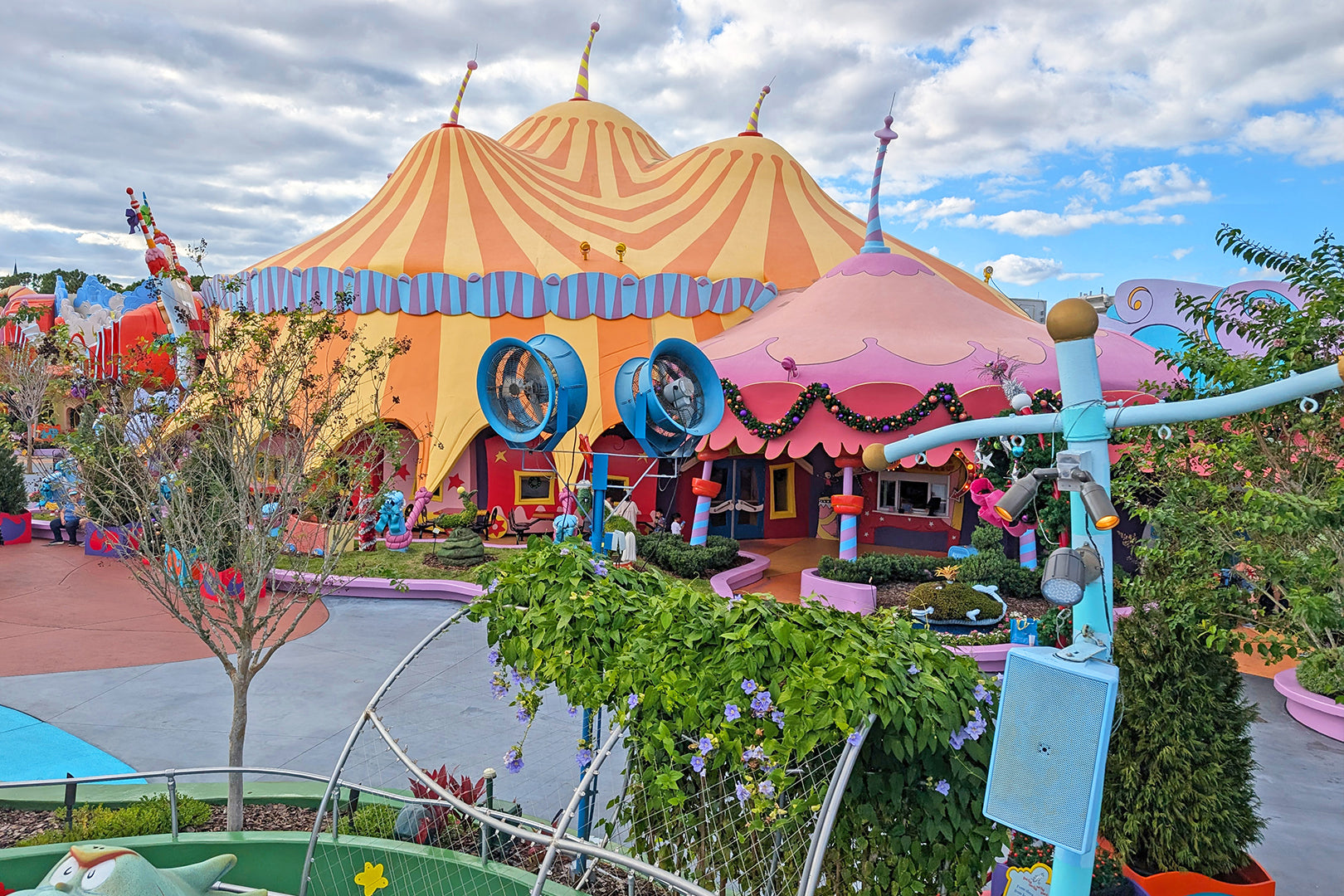 Colorful, whimsical theme-park building with large mounted ventilation fans and decorative landscaping