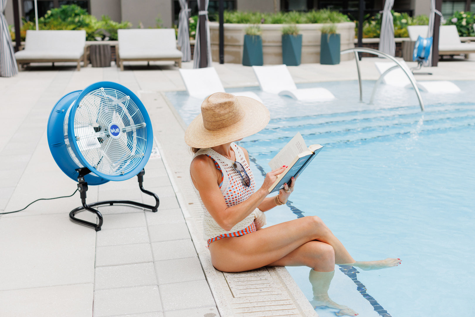 Blue Air portable cooling fan set up beside a pool providing airflow while someone relaxes and reads