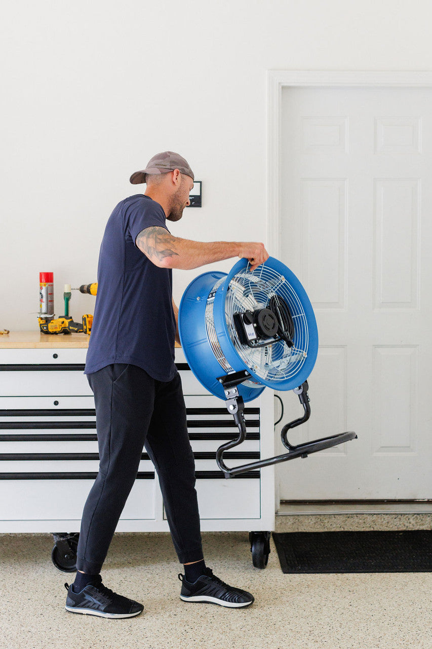 Man adjusting a blue portable floor fan in a garage workspace