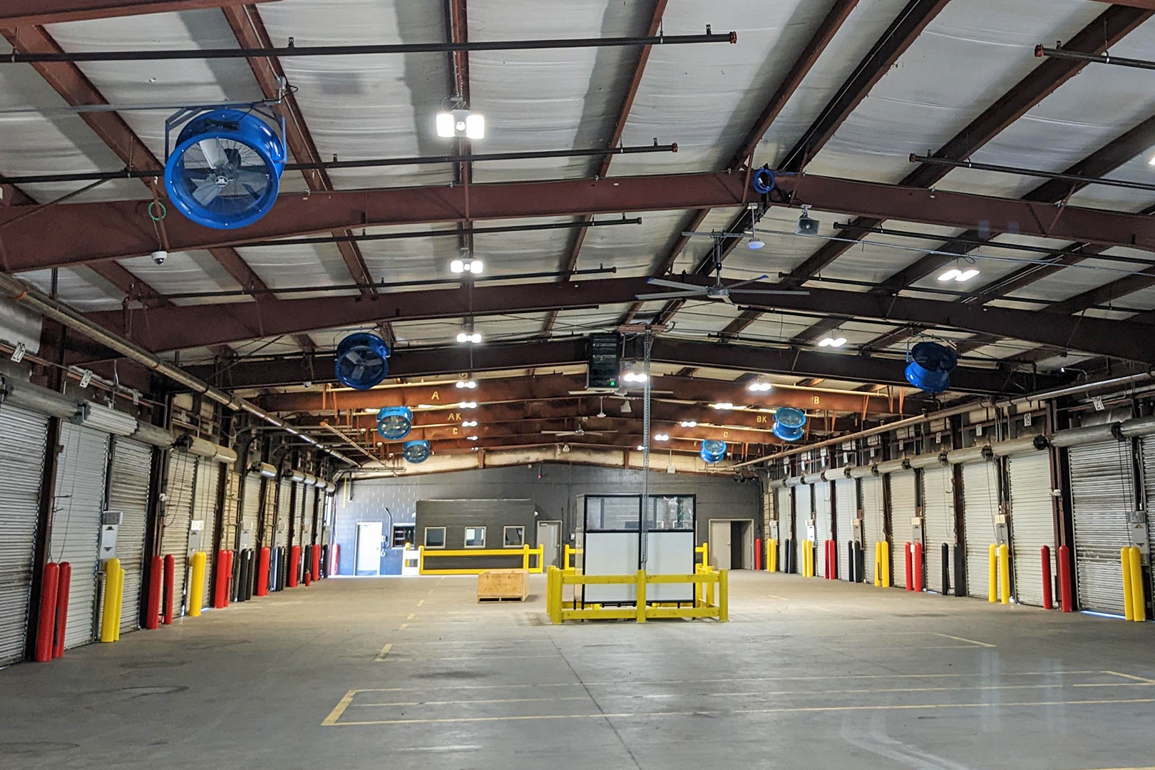 Industrial warehouse interior with multiple mounted blue Patterson high-velocity fans installed along the ceiling for airflow and ventilation