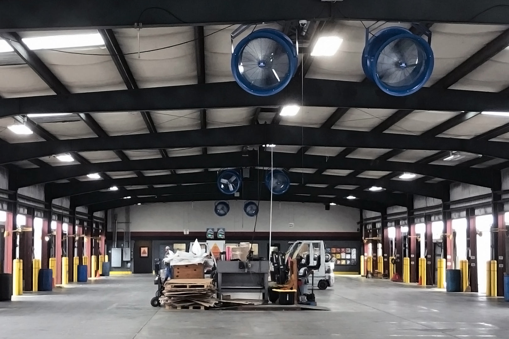Industrial warehouse interior with multiple ceiling-mounted Patterson high-velocity blue fans providing air circulation above loading dock bays
