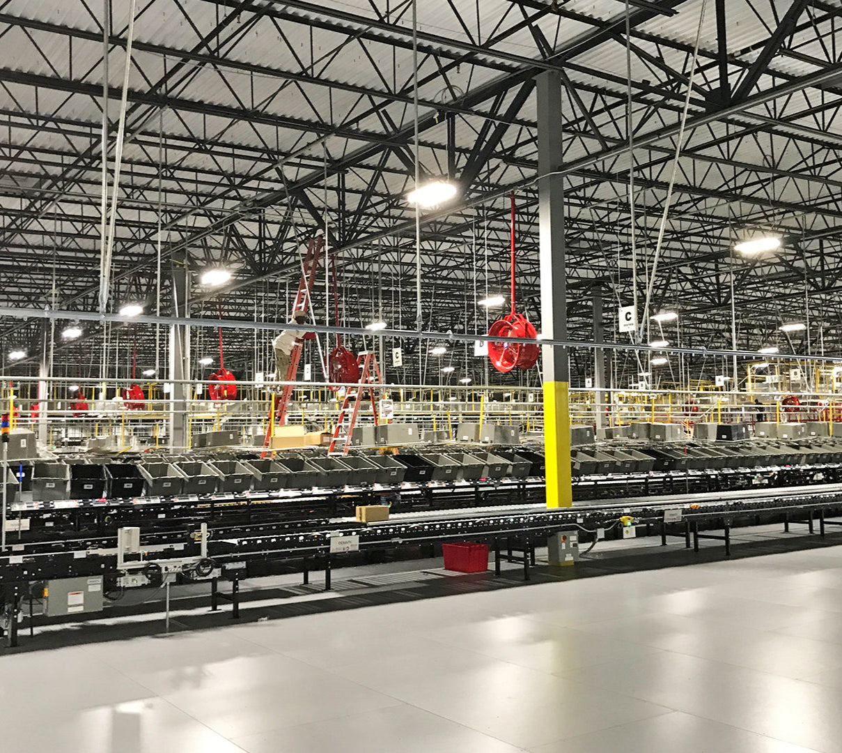 Large warehouse with conveyor systems and red industrial overhead fans for air circulation