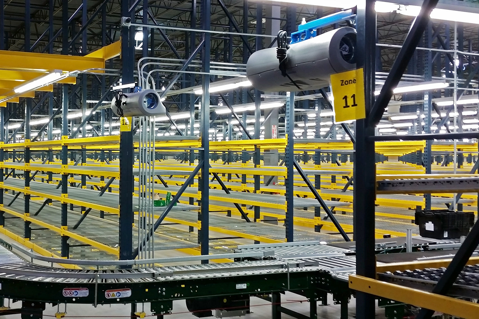 Industrial barrel fans mounted above conveyor system in a warehouse Zone 11 for targeted airflow and worker cooling