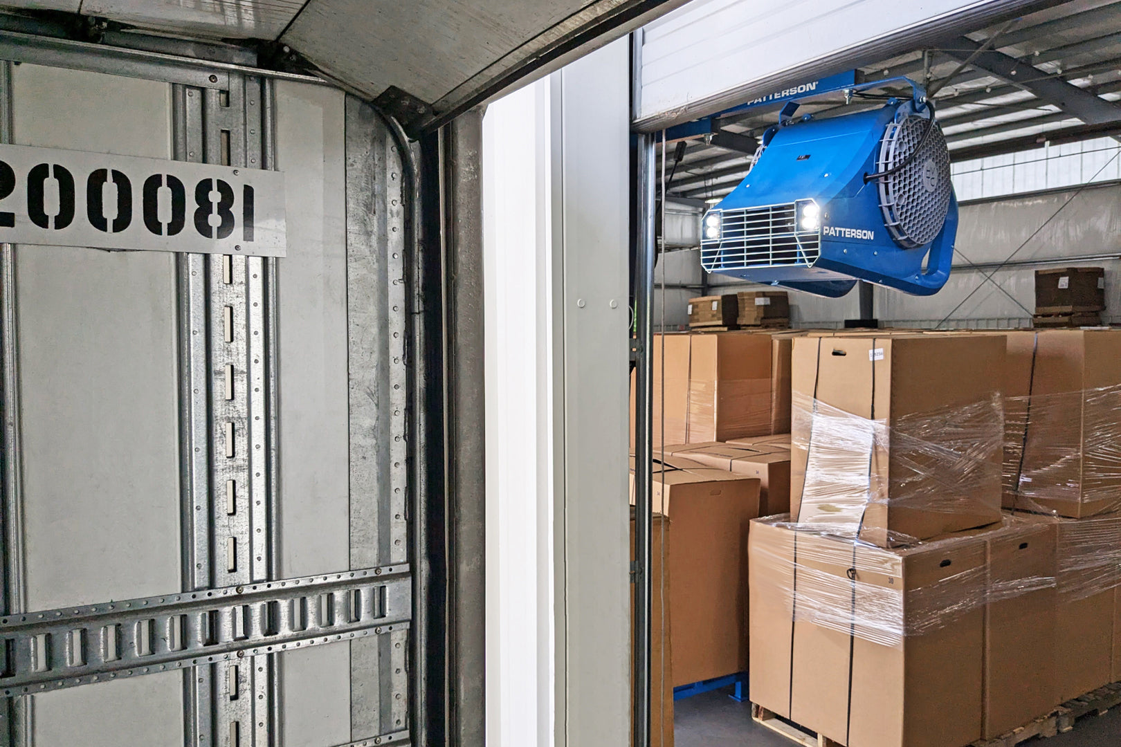 Patterson loading dock door fan mounted above warehouse doorway blowing air into truck trailer with boxed pallets