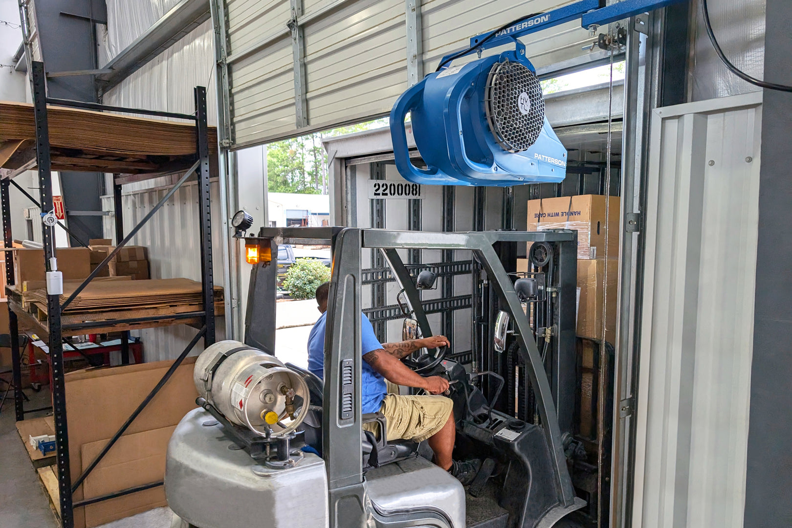Forklift driver loading a trailer beneath a mounted blue Patterson loading dock fan