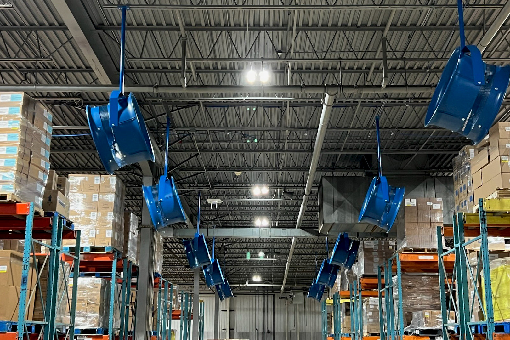 Row of industrial high-velocity blue barrel fans mounted from warehouse ceiling for improved airflow and ventilation