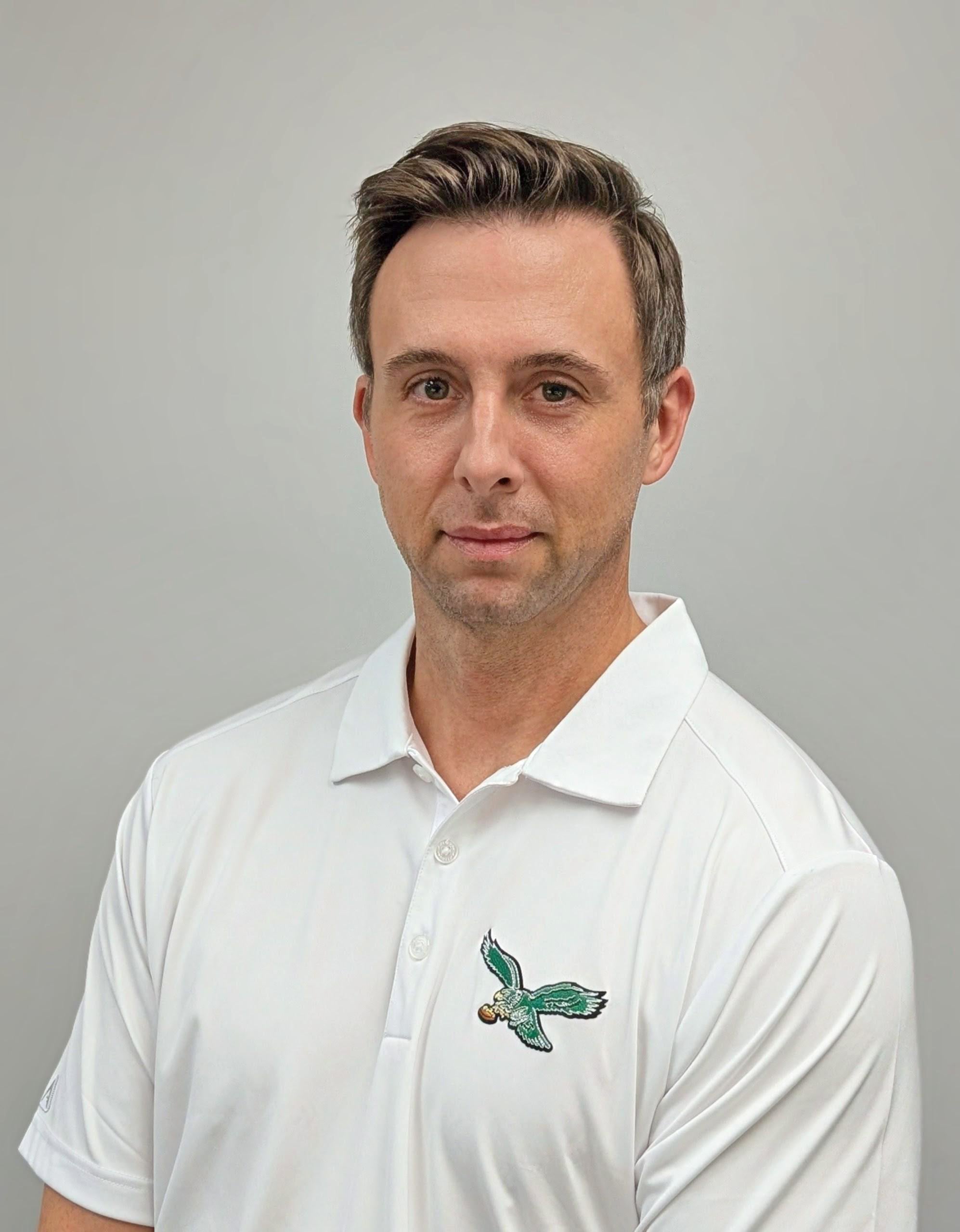 Professional headshop of a man wearing a white polo shirt with a green eagle logo