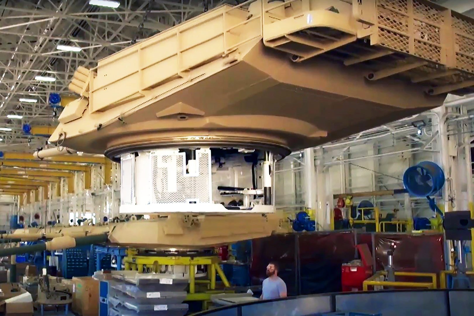 Large industrial manufacturing facility with heavy equipment being assembled and high-velocity blue industrial fans providing air movement