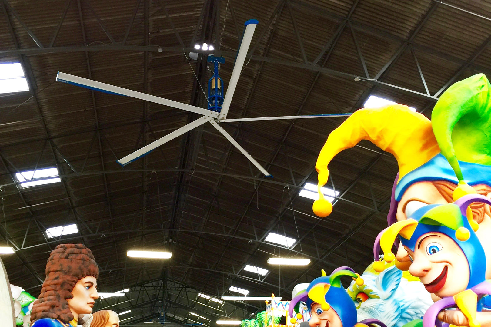Patterson industrial HVLS ceiling fan circulating air in a warehouse filled with brightly colored parade floats