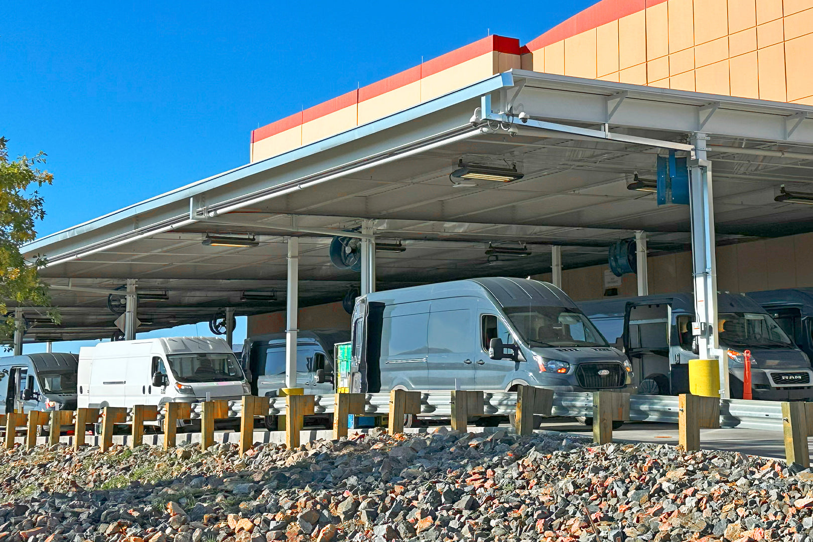 Industrial blue barrel fans mounted under loading dock canopy to improve ventilation for delivery van staging area