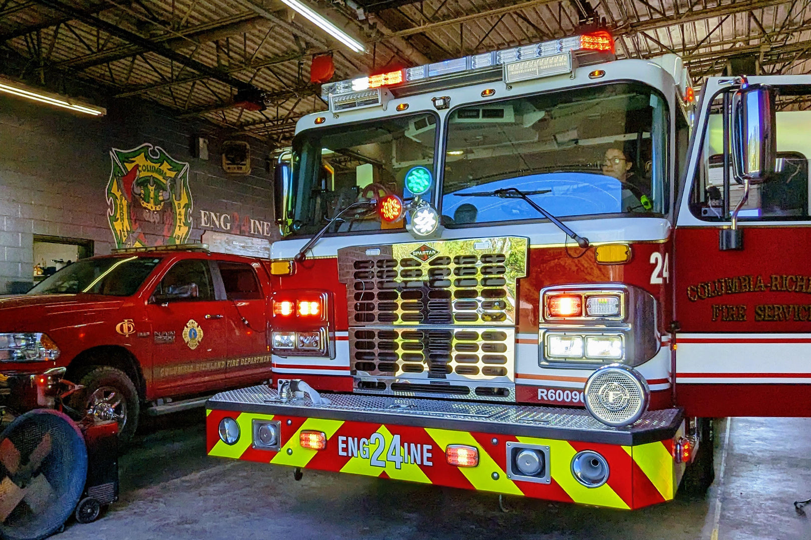 Industrial portable blower fan positioned in a fire station beside fire engines, improving ventilation and air movement