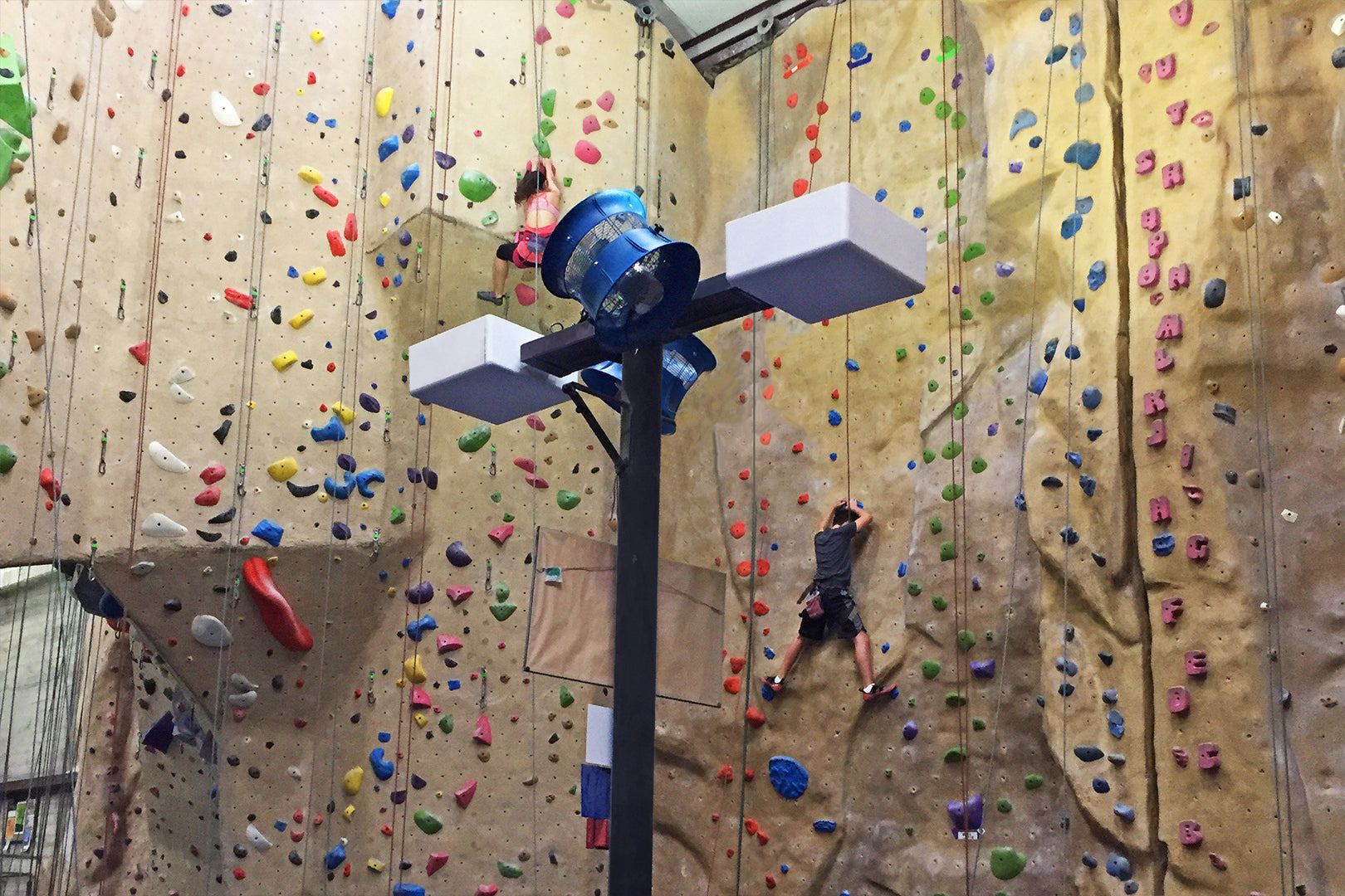 Mounted industrial blue circulation fan installed in an indoor rock climbing gym for improved airflow