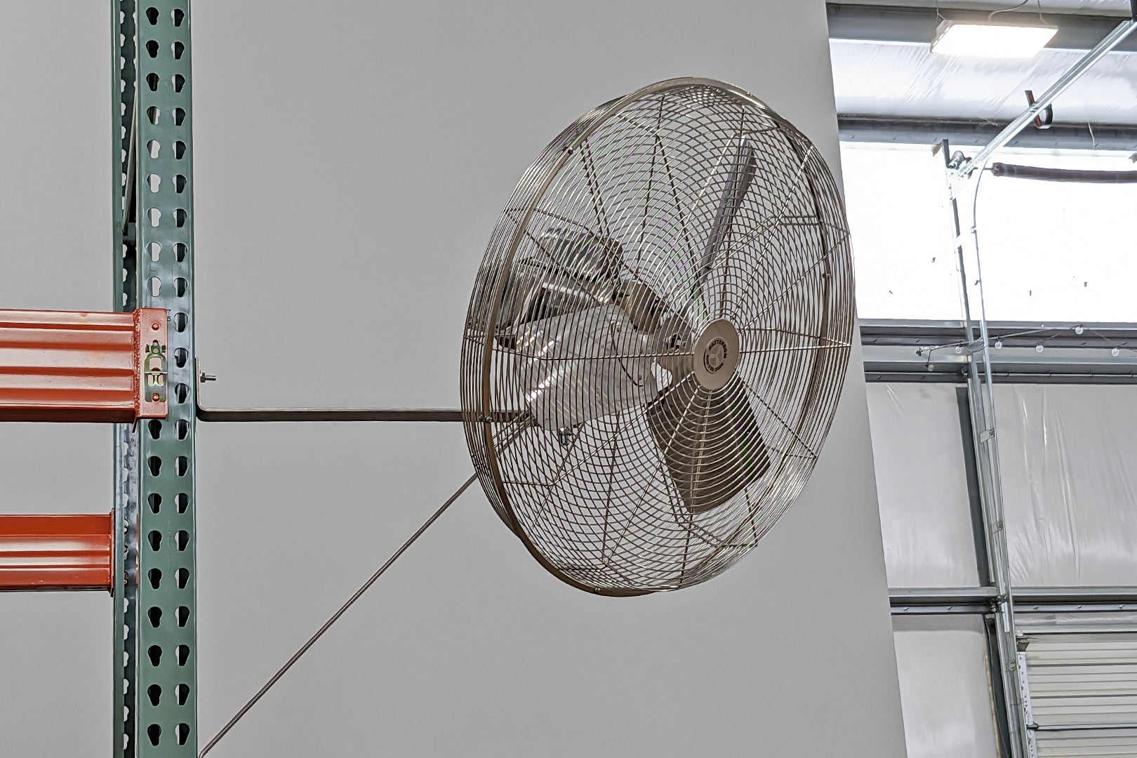 Mounted Patterson industrial stainless-steel fan with protective safety grille on warehouse wall