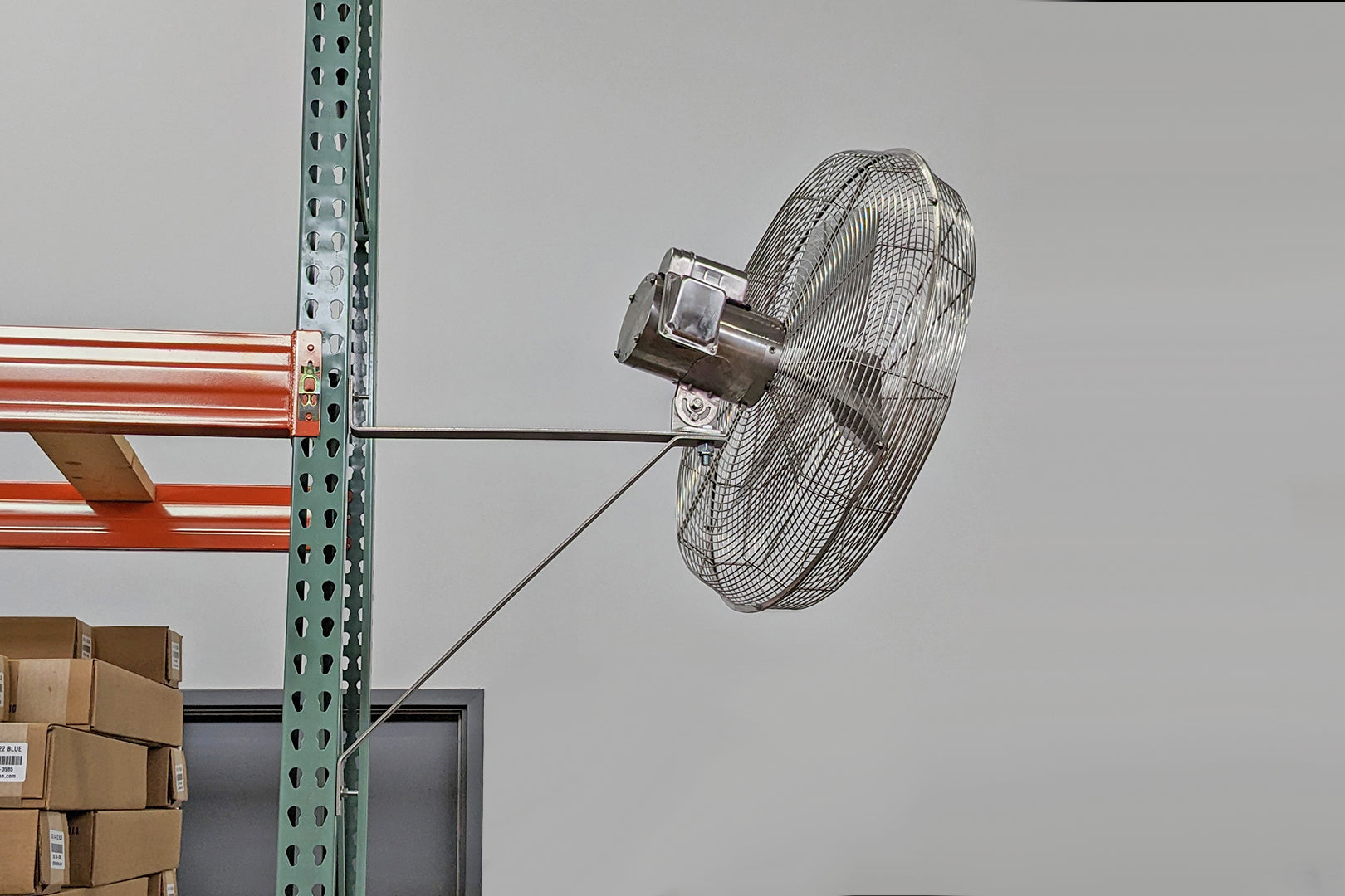 Wall-mounted industrial cage fan attached to warehouse racking for targeted air movement