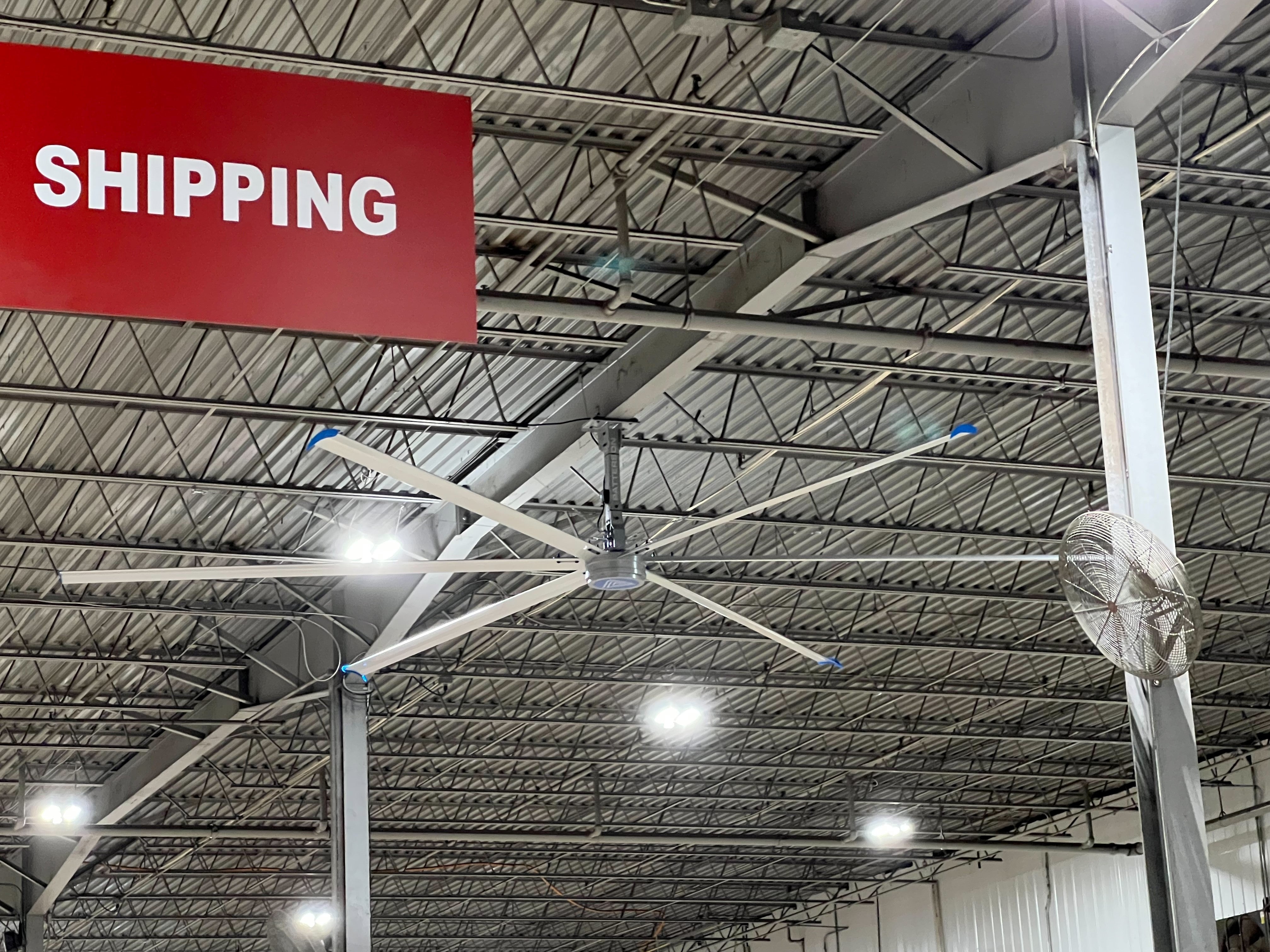 Large industrial ceiling fan and overhead lighting in a warehouse shipping area with a red 'SHIPPING' sign