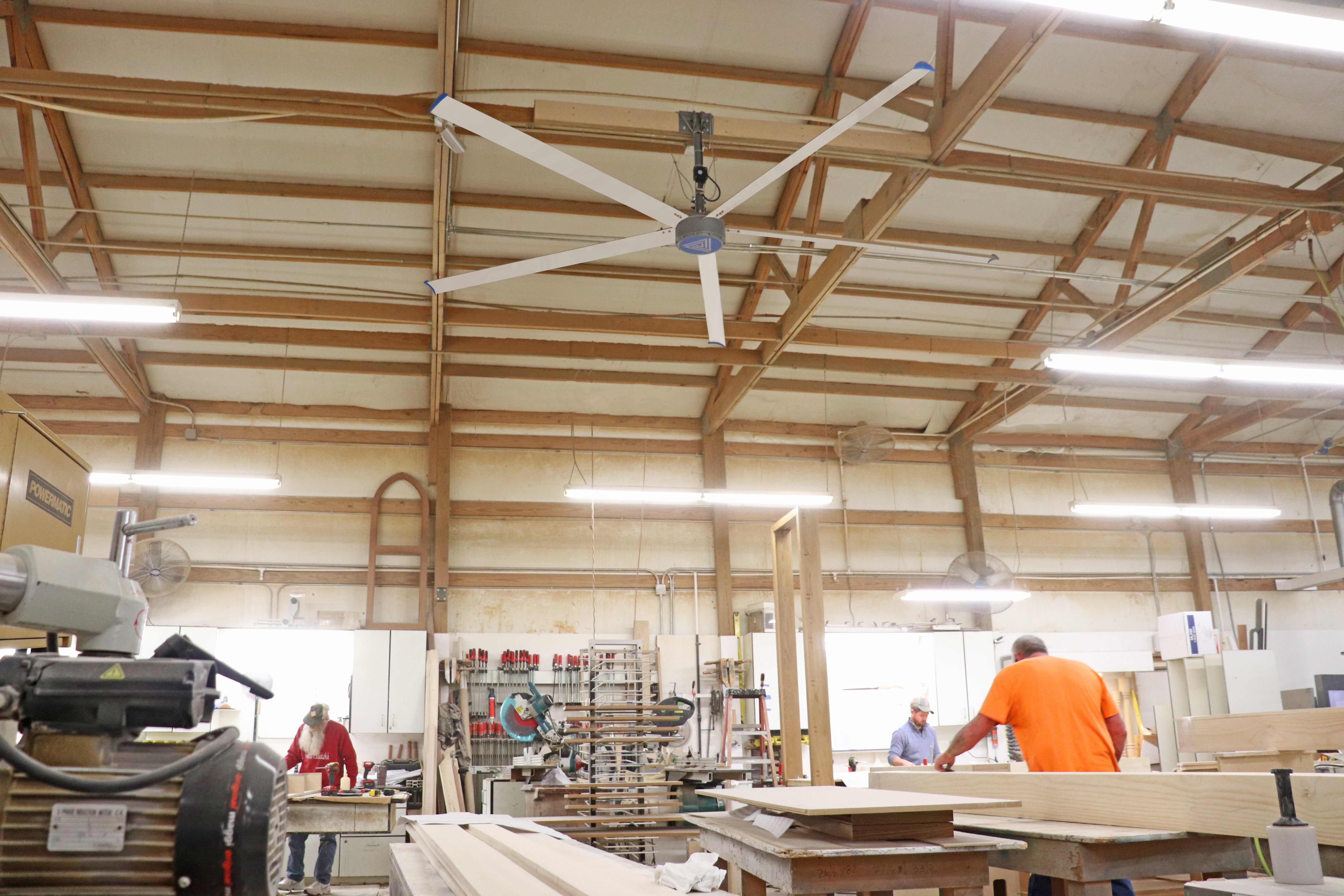 Large HVLS ceiling fan providing airflow in a busy woodworking shop with workers and equipment