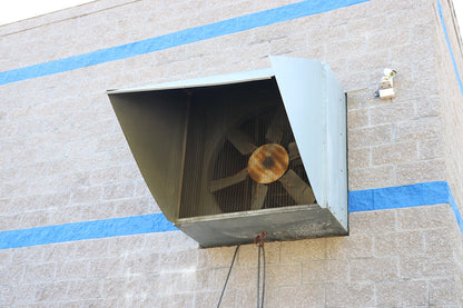 Exterior wall-mounted industrial exhaust fan with protective hood and metal mesh on brick building