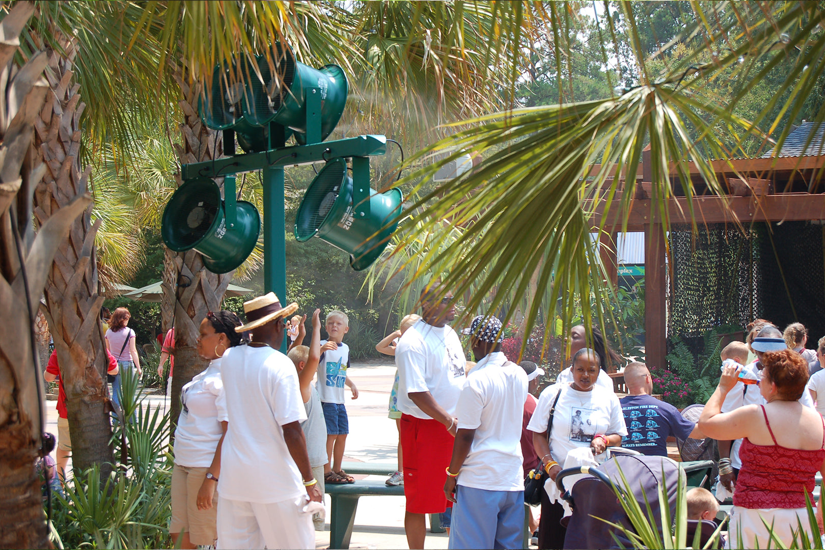 Outdoor green cooling fans mounted on a pole providing airflow in a shaded theme park queue area